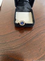 Front view of the 10k gold ring in black box showing the blue center stone and surrounding colorless stones.