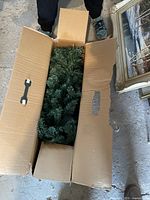 Unopened cardboard box containing artificial Christmas tree in dark green needles.