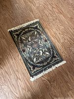 Top-down photo of small rectangular area rug on wooden floor showing design and fringes on one end.