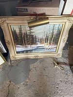 Framed birch forest painting with light fixture, cream ornate frame, viewed from front.