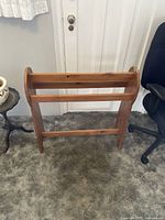 Front angled view of solid wood blanket/quilt stand on carpeted floor, showing horizontal bars and side panels.