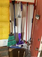 Wide view of cleaning tools lined against a wall including brooms, mops, and plungers.