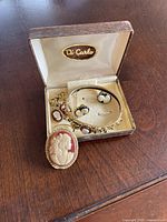Vintage cameo jewelry lot displayed inside original Di Carlo box on wood surface.