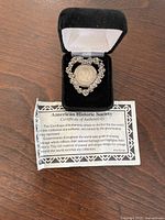 Heart-shaped silver-tone pendant necklace displayed in black velvet box with certificate of authenticity visible.