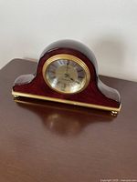 Front view of the small decorative mantel clock showing the clock face with Roman numerals and brass bezel.