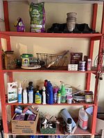Four red metal shelves loaded with various gardening supplies, pest control products, cleaning bottles, and household hardware items.