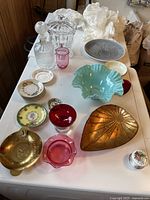 Overview of lot showing crystal decanter, lidded jar, pink glass vase, green ruffled bowl, brass leaf dish, red and pink glass bowls, and several small porcelain dishes and plates.