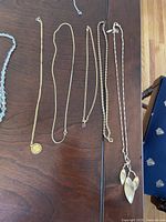 Five gold tone necklaces laid out on a wooden table showing chain and pendant details.