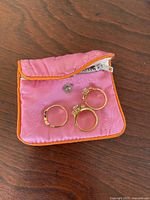 Three gold tone rings displayed on a pink fabric pouch with orange trim on wooden surface
