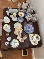 Overview of a variety of ceramic, porcelain, and crystal decorative items on a dark wood table.