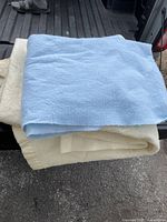 Two large wool blankets stacked; visible light blue blanket on top and cream-colored blanket beneath, showing texture and size.