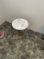 Side view of the round marble top side table with detailed brass base on carpeted floor