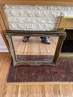 Full view of the ornate framed mirror standing on the floor, showing the detailed floral and scrollwork decorations on the frame and clear reflection in the glass.