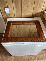 Mirror placed horizontally on a white surface against wood panel wall, showing the frame texture and reflection.