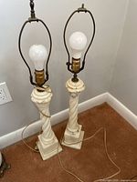 Two tall marble lamps showing twisted column design, light sockets with bulbs, electrical cords, square bases.