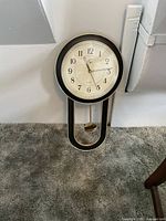 Full view of the Eya wall pendulum clock placed against a wall and carpeted floor.