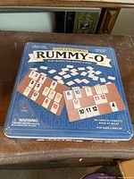 Top view of the metal storage box for Rummy-O Collector's Edition game, showing tile racks and various numbered tiles.