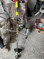 Full view of RYOBI 40V cordless string trimmer with loop handle resting on camo patterned chair inside a garage/storage area.