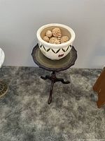 Small antique wooden tripod side table with scalloped edge top holding a ceramic pot filled with carved wood balls.