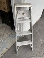 Side view of aluminum step ladder showing four steps, metal braces, and folding hinge with paint marks and scuffs.