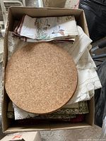 Top view of a box with folded tablecloths, table runners, and two round cork trivets placed on top