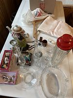 Overview of the lot showing tablecloth, teapot, various glassware items, and boxes with jewellery on white table.
