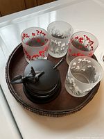 Photo showing round wooden tray holding four frosted glasses decorated with red and white berry branches and a dark metal drink accessory set.