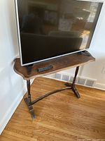 Full view of wooden TV stand with a TV and remote on top, positioned near a wall corner on hardwood floor.