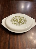 Closed view of vintage white Pyrex platter with lid featuring green Spring Blossom pattern on lid