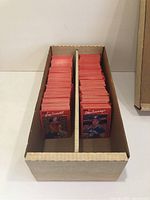 Two photos showing a cardboard box filled with organized 1990 Donruss baseball cards. The cards have red borders and feature players on the front.