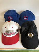 Four NHL baseball-style hats: two Winnipeg Jets (blue), one Montreal Canadiens (white/red), one Boston Bruins (black mesh)