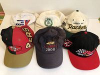 Top view of 6 sports hats including NFL, NBA, golf and racing themed caps in varying colors.