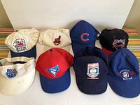 Photo showing 8 MLB baseball caps with various team logos, primarily Blue Jays caps.
