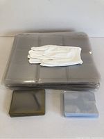 Photo shows one stack of transparent protective sheets, one stack of transparent rigid card holders, one stack of tinted rigid card holders, and one pair of white fabric gloves on top of the sheets.