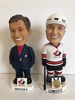 Front view of both bobblehead figures, Gretzky in blue suit and Lemieux in hockey gear.