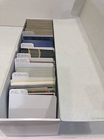 White storage box filled with sets of neatly organized baseball cards separated by labeled dividers for years and brands including 87 O-Pee-Chee, 87 Donruss, 90 Topps, 90 Bowman, and miscellaneous 90s cards.