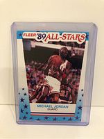 Front side of Michael Jordan 1989 Fleer All-Star basketball card in protective plastic case. Shows player in Chicago Bulls uniform mid-air with basketball, surrounded by blue star-patterned border.