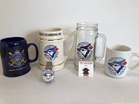 Four Toronto Blue Jays mugs, one silver-tone wrist watch, and one enamel pin with Blue Jays mascot.