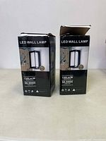 Two boxed LED wall lamps placed side by side, front view showing product image and features.