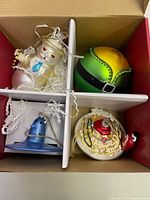 Photo of four Christmas ornaments placed in a divided white tray, showing a snowman, Santa hat, blue bell, and spaghetti plate ornament.