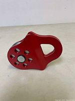 Front angled view of a red painted heavy duty towing pulley showing the metal pulley wheel and multiple holes in red side casing.