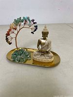Front angled view showing Buddha statue seated next to colorful chakra crystal tree on gold tray.