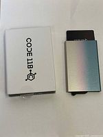 CODE 118 aluminum wallet with metallic gradient finish and white branded box, shown from top and inside the box.