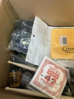 Photo of large box showing various music accessories including drumsticks, Ernie Ball guitar strings, and a package labeled CineMag.