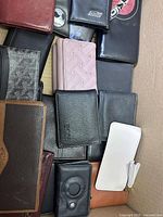 Top view of assorted wallets in a box showing a variety of styles and colors including black, brown, pink, and white wallets.