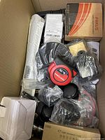 Top-down view of box showing mix of cables, measuring tape, and boxed item labeled 'Focus'. Several items are in plastic packaging or sealed bags.
