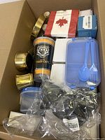 Top view of large box showing brass candle holders, Tiger-Cats cup, blue plastic lunchbox with utensils, several small bags of items, and a packaged red maple leaf item