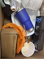 View of assorted items including blue tumbler, orange accessories, white dish and water filter in box