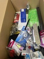 View inside the large box showing rulers, sewing kits, rotary cutter, measuring tools, and other miscellaneous craft and office items, most appearing new or lightly used.