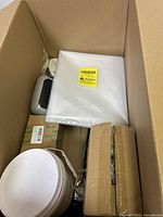 Box with sealed packs of white material, a portable heater or fan, and a small cardboard box.